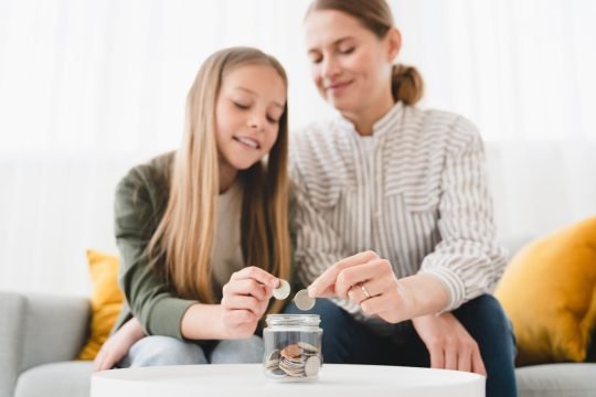 Smiling happy caucasian family of mother and daughter saving money, putting coins into bank, planning future, paying bills loan together. Nest egg concept.